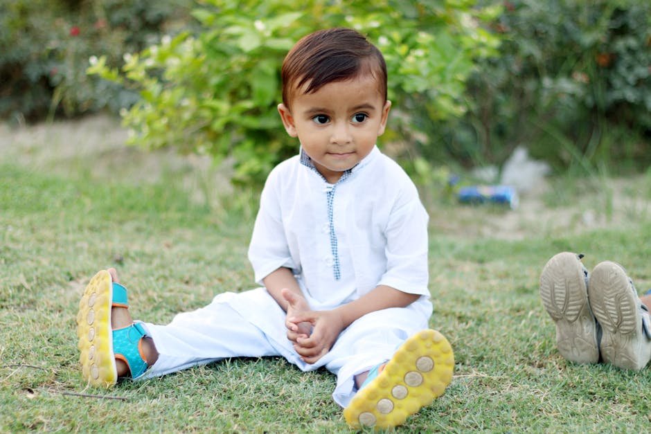 Boys best dresses in Pakistan - Cute toddler in white attire sitting on grass in Mian Channu, Pakistan.