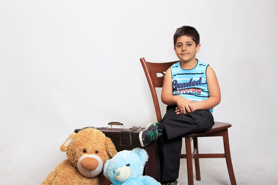 a young boy sitting on a chair next to a teddy bear