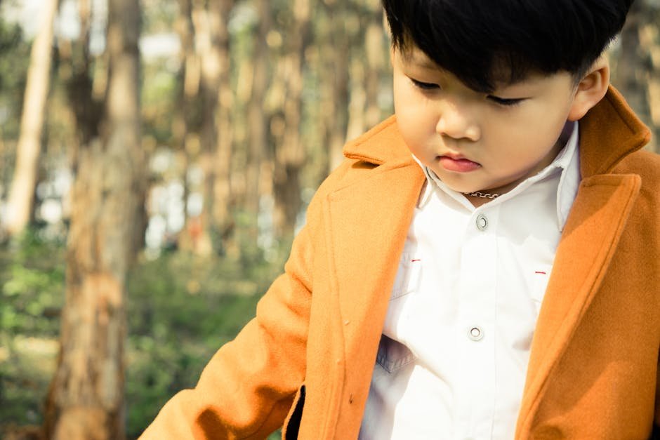 Boys dresses unique collection - A fashionable young boy in a fall forest wearing a stylish orange coat.